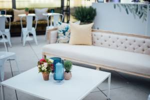 Photograph of event furniture rentals used at a garden wedding. there are metal tolix chairs in the background with small tables all white, a nice comfortable couch and coffee table with center piece in the front.