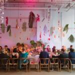 Floral arrangements hanging on the ceiling above a long table with guests seated.