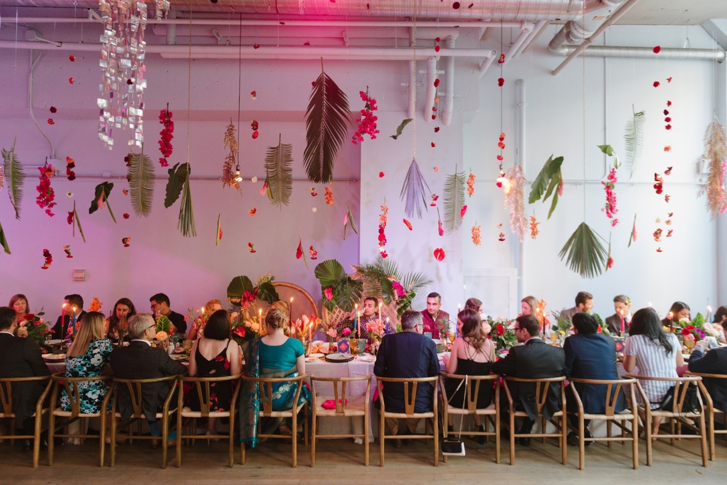 Floral arrangements hanging on the ceiling above a long table with guests seated.