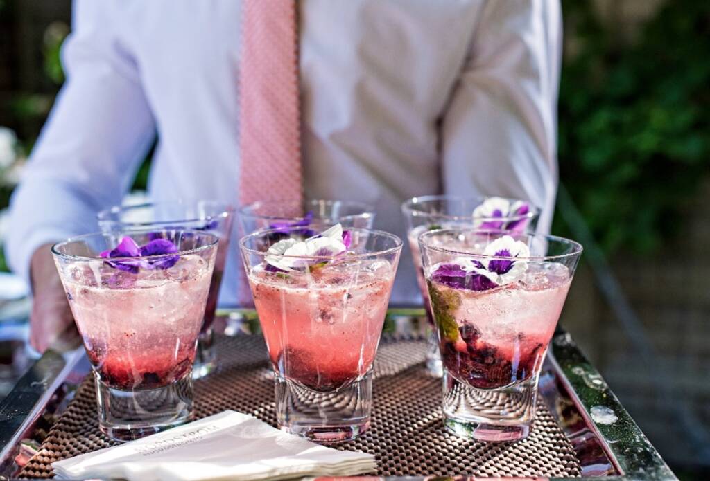 Pink drink with purple florals being passed on a silver tray.