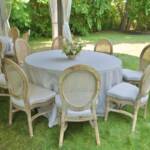 Elegant round table with white table cloth and chairs set in a grassy backyard under a canopy tent to be used for dinner service for a backyard wedding