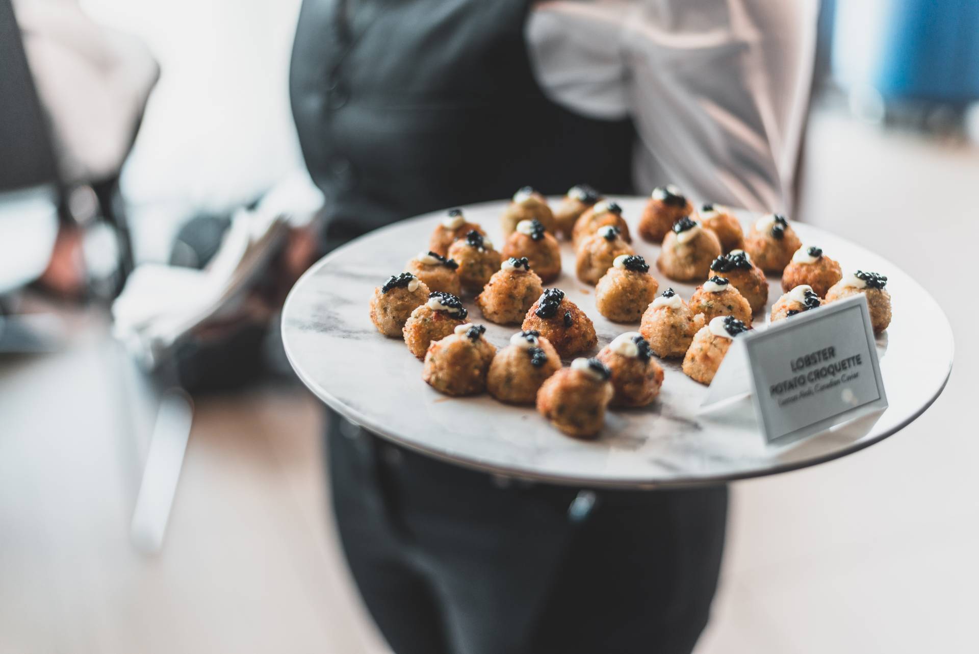 Server holding a marble platter with Lobster Potato Croquettes on top